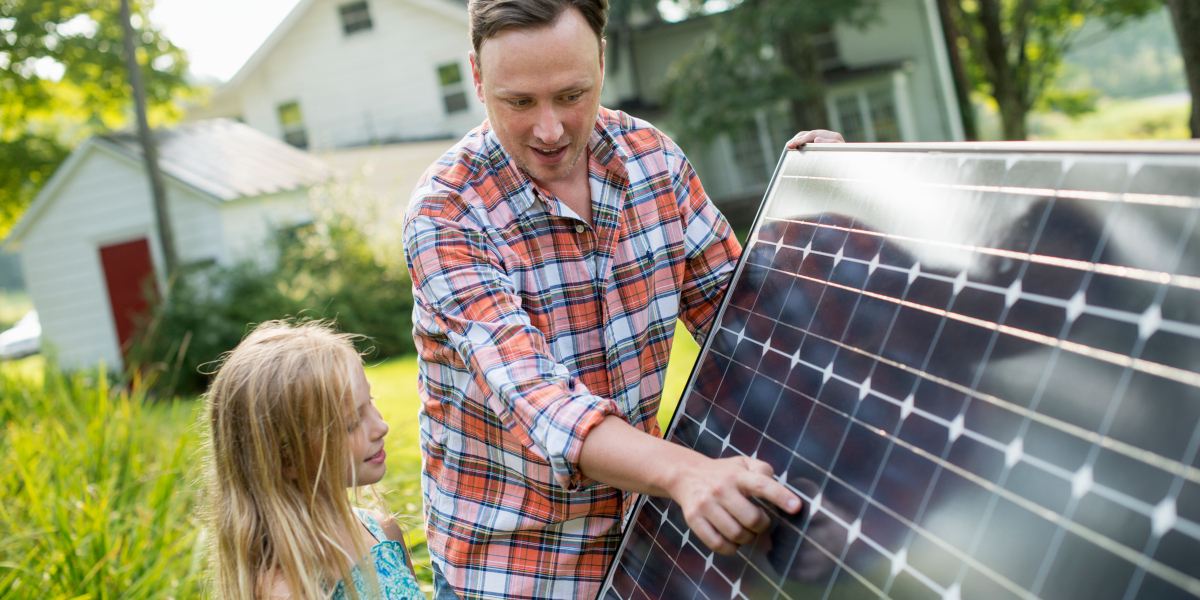 A man and a young girl looking at a solar panel in a garden.